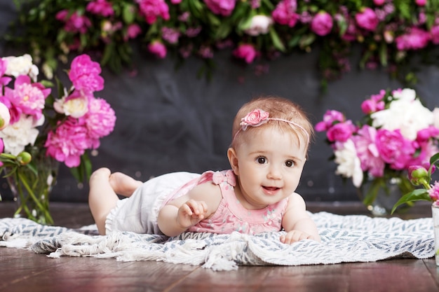 Foto portret van een mooi klein babymeisje met roze bloemen. lief glimlachend meisje dat op haar buik ligt