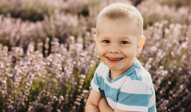 Portret van een mooi klein kind kijken camera met plezier terwijl tong in een veld van bloemen wordt weergegeven bij de zonsondergang.