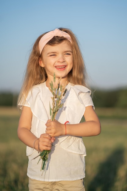 Portret van een mooi klein meisje met blond haar Het kind loopt in het veld en verzamelt een boeket Modelverschijning in een kind