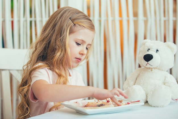 Portret van een mooi klein meisje met een teddybeer in een café dat een heerlijk ijsje eet.