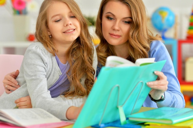 Portret van een mooi klein schattig meisje dat een boek leest met moeder aan tafel thuis