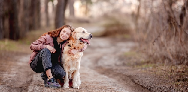 Portret van een mooi meisje dat een golden retriever-hond in het bos knuffelt en glimlacht