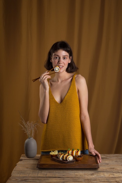Portret van een mooi meisje dat sushi-broodje met zalm eet met stokjes op een gele achtergrond