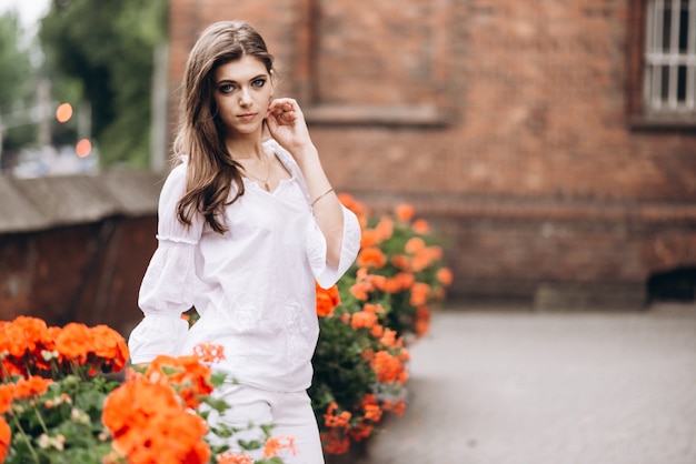 Portret van een mooi meisje gekleed in wit en permanent in de buurt van de bloemen