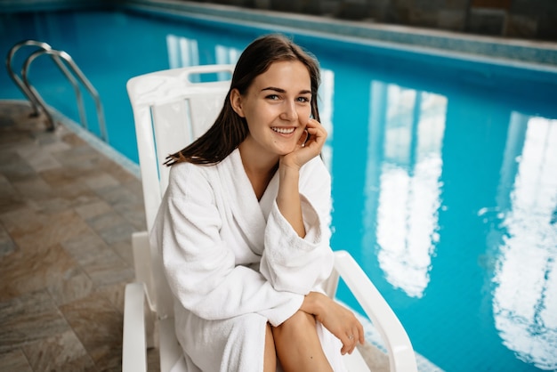 Foto portret van een mooi meisje in een badjas tegen een zwembad