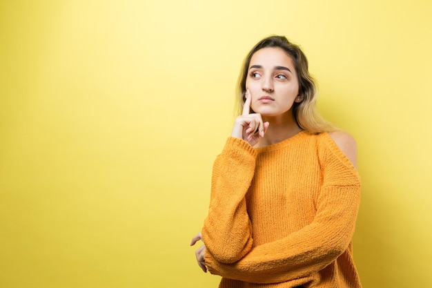 Portret van een mooi meisje in een oranje trui kijkt opzij met peinzende uitdrukking