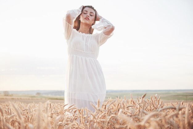 Portret van een mooi meisje in een witte jurk op het gebied van tarwe