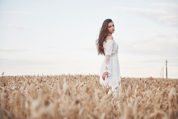Portret van een mooi meisje in een witte jurk op het gebied van tarwe