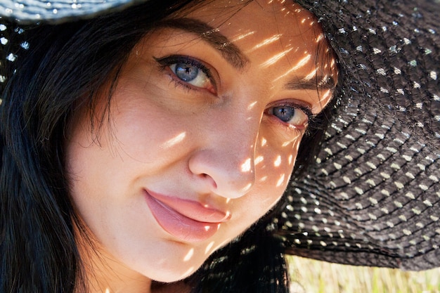 Portret van een mooi meisje met schaduwen in een zwarte hoed op een zonnige dag