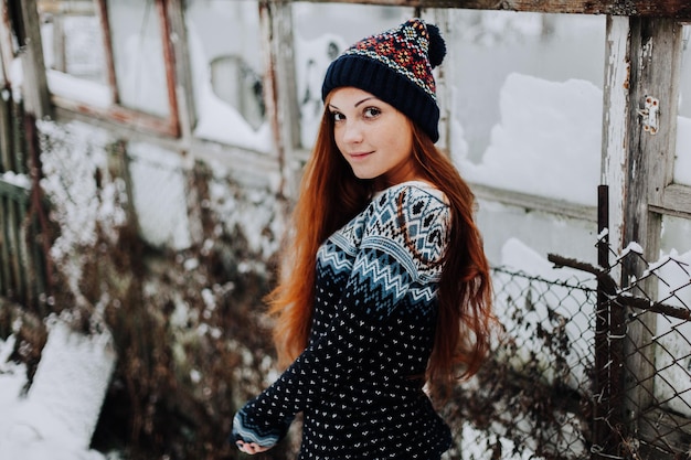 Portret van een mooi meisje met sproeten met lang rood haar en een schattige charmante glimlach met een grijze stijlvolle hoed die kijkt en glimlacht naar de camera die tegen de achtergrond van de studiomuur staat Geïsoleerd schot horizontaal