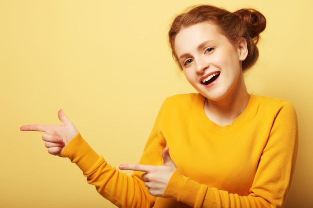 Portret van een mooi redhairmeisje die vinger richten weg over gele achtergrond