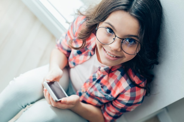 Portret van een mooi vrolijk meisje met een bril die vrolijk lacht terwijl ze een moderne smartphone vasthoudt