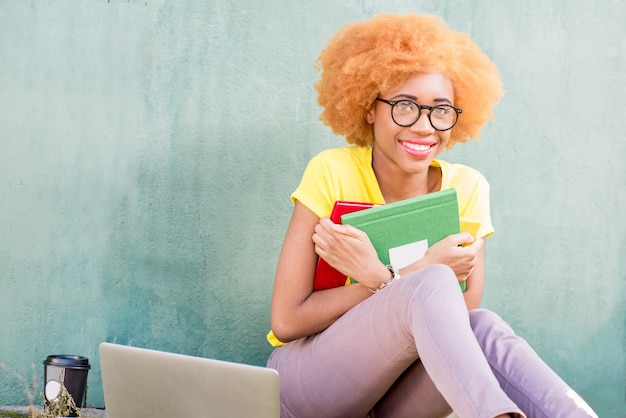 Portret van een mooie Afrikaanse student met kleurrijke boeken op de groene muurachtergrond