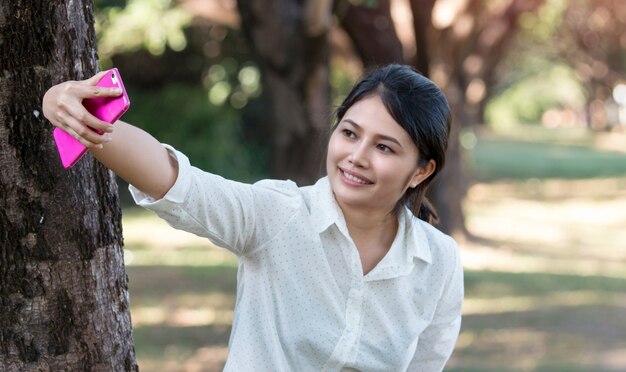 Portret van een mooie Aziatische jonge vrouw selfie in het park met een smartphone.