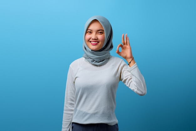 Portret van een mooie aziatische vrouw die lacht en een goed teken doet met de hand op een blauwe achtergrond