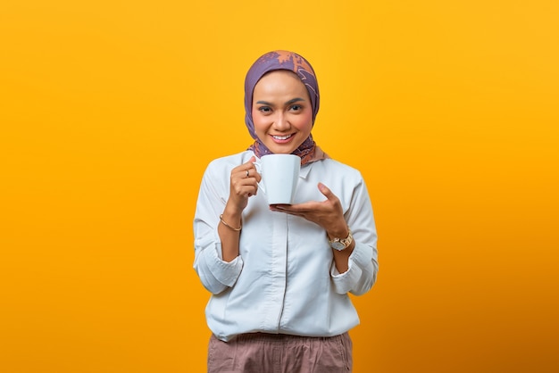 Portret van een mooie Aziatische vrouw die lacht en een mok vasthoudt op een gele achtergrond