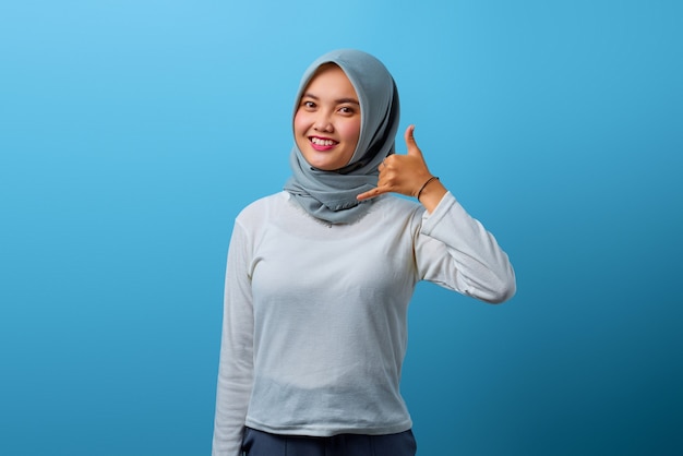 Portret van een mooie Aziatische vrouw die lacht en een telefoongebaar doet met de hand op een blauwe achtergrond