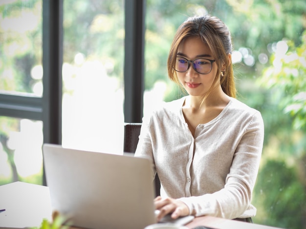 Portret van een mooie aziatische zakenvrouw met een bril die op een laptop op kantoor werkt met wazig natuurlijk op de achtergrond