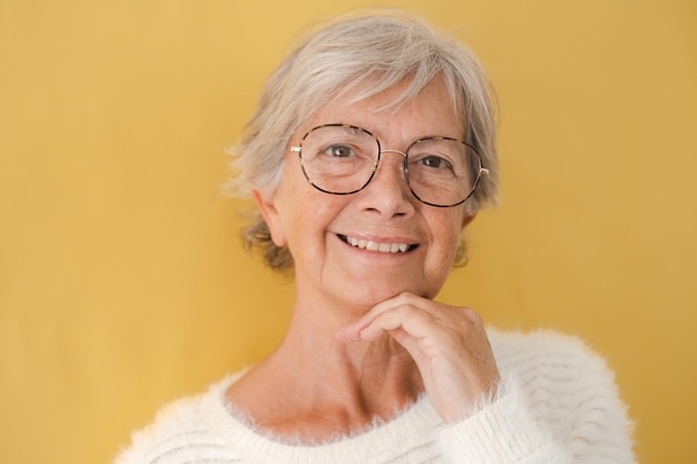 Portret van een mooie blanke senior vrouw in een witte trui en bril die naar een camera kijkt die glimlacht en sereniteit uitdrukt