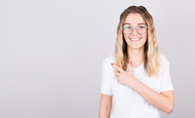 Portret van een mooie blonde meisje wijzende vinger weg geïsoleerd op grijs