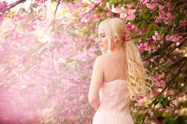 Portret van een mooie blonde tegen een achtergrond van bloeiende sakura