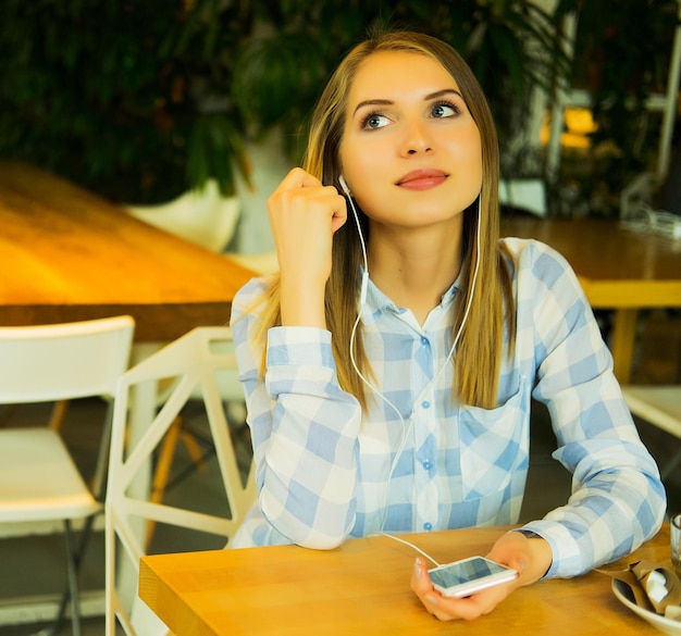 Portret van een mooie blonde vrouw die muziek luistert en een mobiele telefoon vasthoudt in de coffeeshop