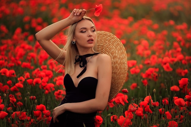 Portret van een mooie blonde vrouw in een strohoed bij zonsondergang op een papaverveld