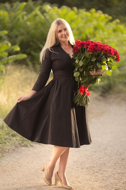 Portret van een mooie blonde vrouw met een groot boeket van honderd rode rozen