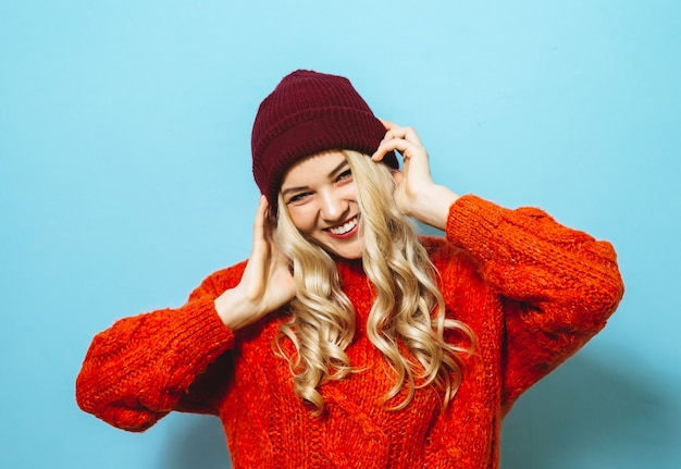 Portret van een mooie blondevrouw die een GLB dragen en is gekleed in een rode sweater en manierbewegingen over blauwe achtergrond tonen