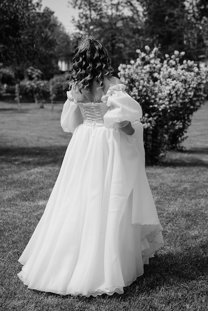 Portret van een mooie bruid in bruidsjurk met een modern kapsel en sluier die op de achtergrond van de tuin loopt Bruidsconcept Bruid die op een zonnige dag in een bos wegloopt Zwart-wit foto