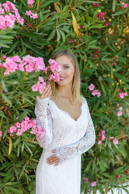 Portret van een mooie bruid in een witte jurk in een struik van bloemen.