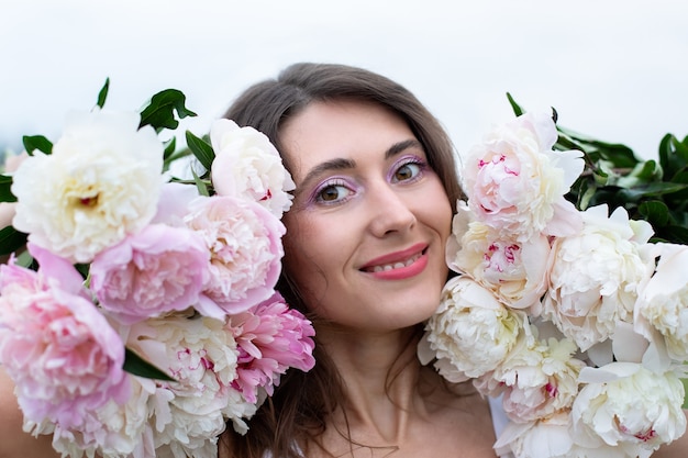 portret van een mooie brunette vrouw tussen pioenrozen glimlachende vrouw met een boeket pioenrozen