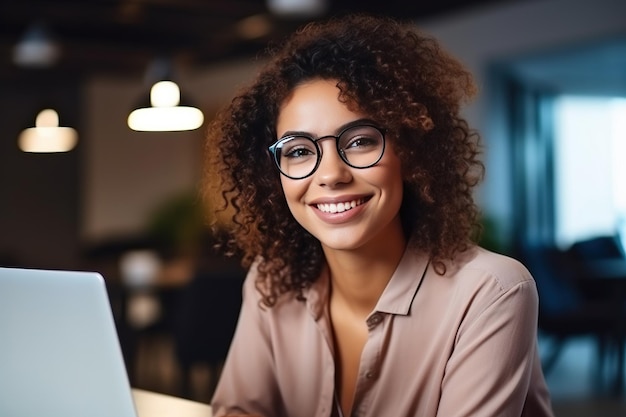 Portret van een mooie, diverse vrouw die een bril draagt en een laptopcomputer gebruikt Kijkt naar de camera en glimlacht Specialist in informatietechnologie Software-ingenieur of ontwikkelaar Generatieve AI