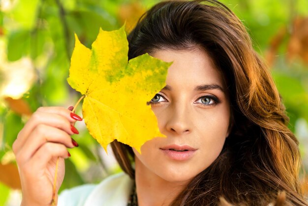 Portret van een mooie en lieve jonge vrouw die gevallen blad vasthoudt en in het park poseert