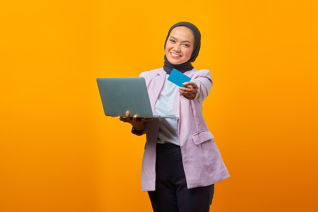 Portret van een mooie en vrolijke jonge vrouw die een laptop vasthoudt en een creditcard toont