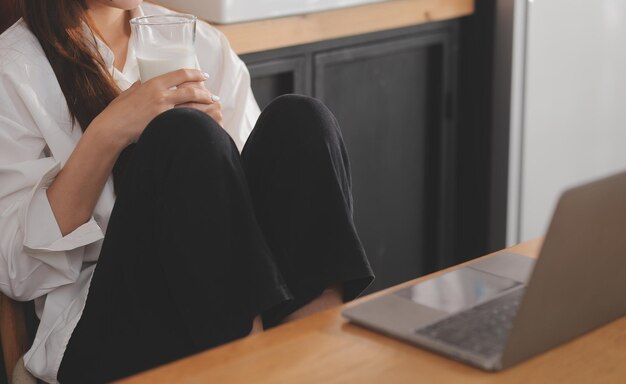 Portret van een mooie freelancer vrouw die aan het typen is op een laptop, aan tafel zit, glimlacht en naar een scherm kijkt in de keuken, aantrekkelijke roodharige jonge vrouw die op afstand aan een laptop werkt vanuit haar kantoor thuis.