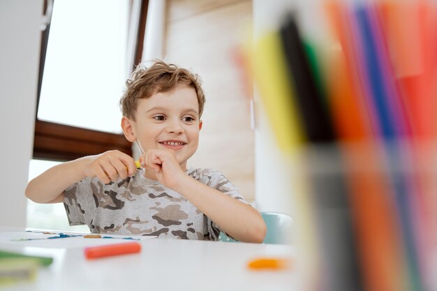 Portret van een mooie, gelukkige jongen die aan de keukentafel zit te genieten van wat vrije tijd weinig