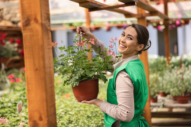 Portret van een mooie glimlachende bloemistenvrouw die met bloemen in een serre werkt.