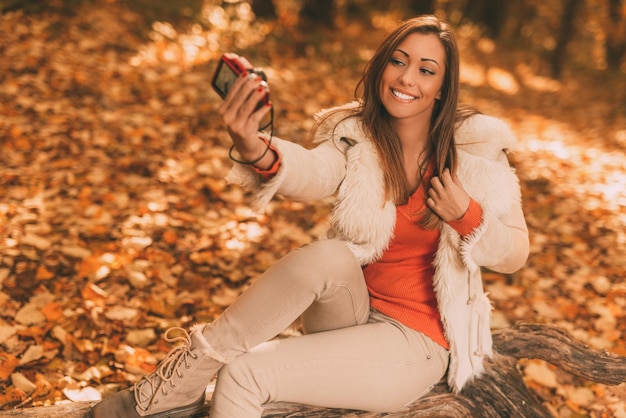 Portret van een mooie glimlachende vrouw die selfie in het bos neemt in de herfst.