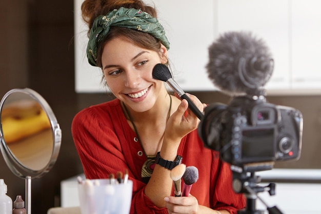 Foto portret van een mooie glimlachende vrouwelijke vlogger maakt video recensie gebruikt cosmetische producten records nuttige inhoud voor blog online succesvolle vrouwelijke blogger werkt aan verbetering van sociale netwerken