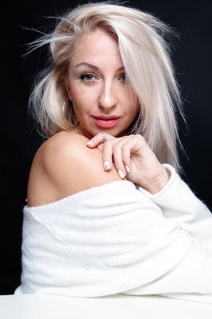 Portret van een mooie jonge aantrekkelijke vrouw in een witte trui met blauwe ogen en lang blond haar.