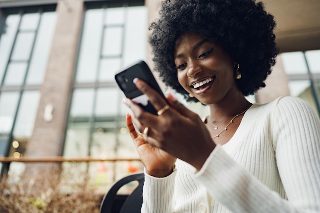 Portret van een mooie jonge Afrikaanse vrouw die haar mobiele telefoon gebruikt in een café