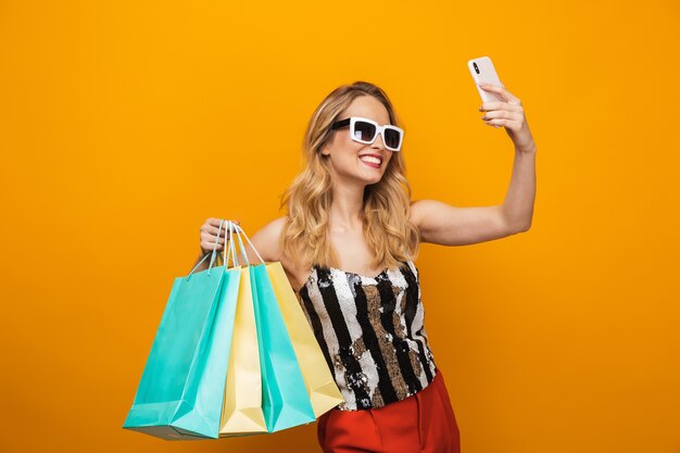 Portret van een mooie jonge blonde vrouw geïsoleerd op gele achtergrond, een selfie te nemen