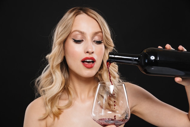 Portret van een mooie jonge blonde vrouw met lichte make-up rode lippen poseren geïsoleerd drinken van rode wijn.