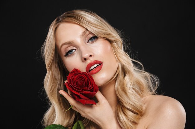 Portret van een mooie jonge blonde vrouw met lichte make-up rode lippen poseren geïsoleerd houden roze bloem.