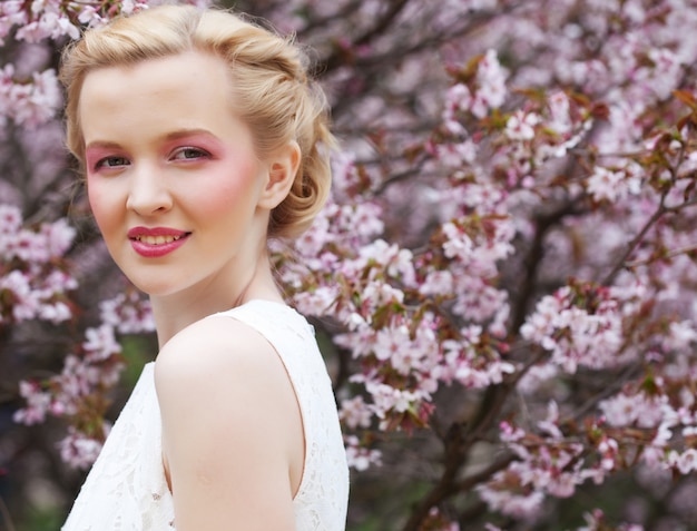 Portret van een mooie jonge blonde vrouw op a van roze kersenbloesems in de lente