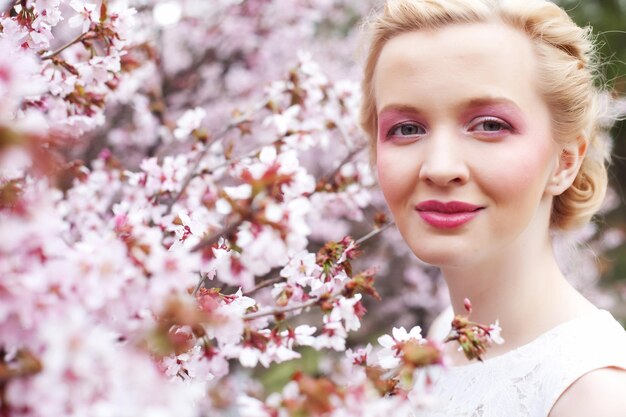 Portret van een mooie jonge blonde vrouw op een achtergrond van roze kersenbloesem in het voorjaar