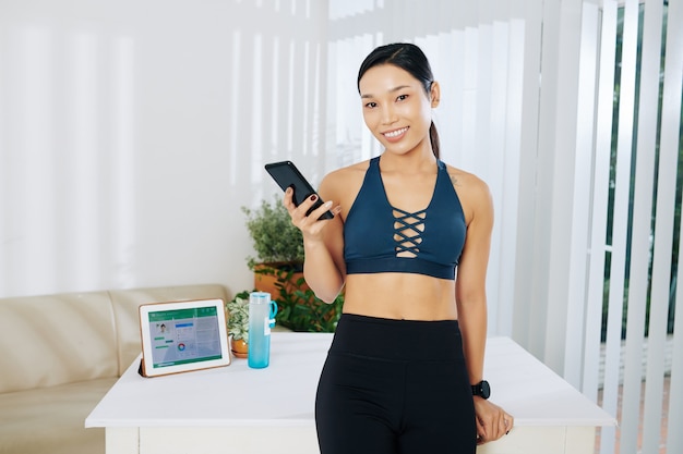Portret van een mooie jonge, fitte Aziatische vrouw met een smartphone die op een tafel leunt met een tabletcomputer met een app voor de gezondheidszorg