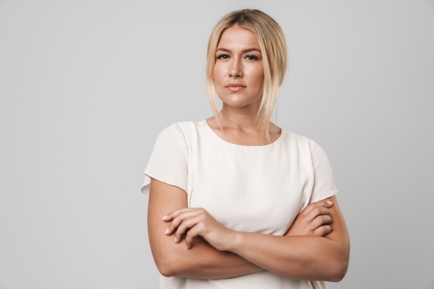 Portret van een mooie jonge geweldige blonde vrouw die zich voordeed over een grijze muur, gekleed in een basic wit t-shirt