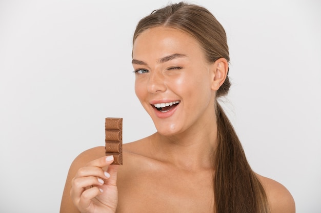 Portret van een mooie jonge topless vrouw met stuk chocolade geïsoleerd, knipogen